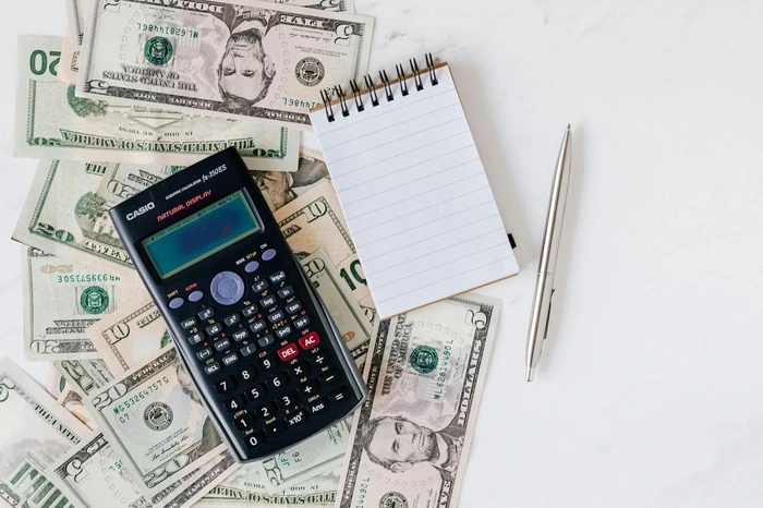 Calculator, notepad, and pen placed on a pile of money