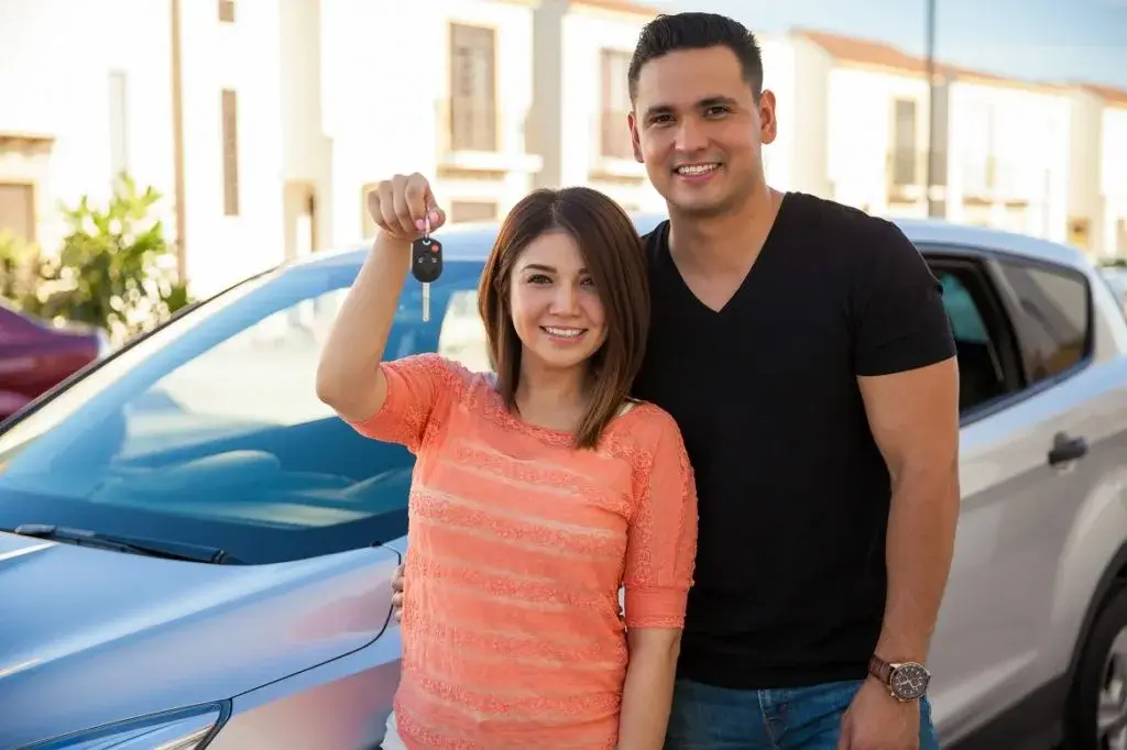 A happy couple stands in front of their car, holding keys, after obtaining SR-22 Insurance in California from Breathe Easy Insurance