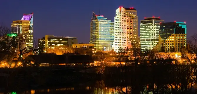 Sacramento skyline at night, with illuminated buildings reflecting off the water in the foreground