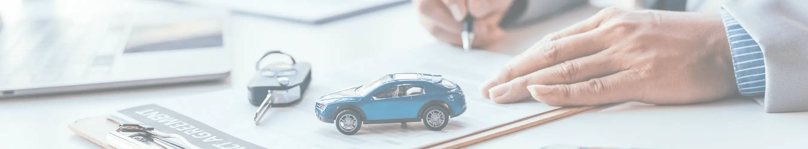 Close-up of a person’s hand writing on paper with a small blue toy car and car keys on the desk