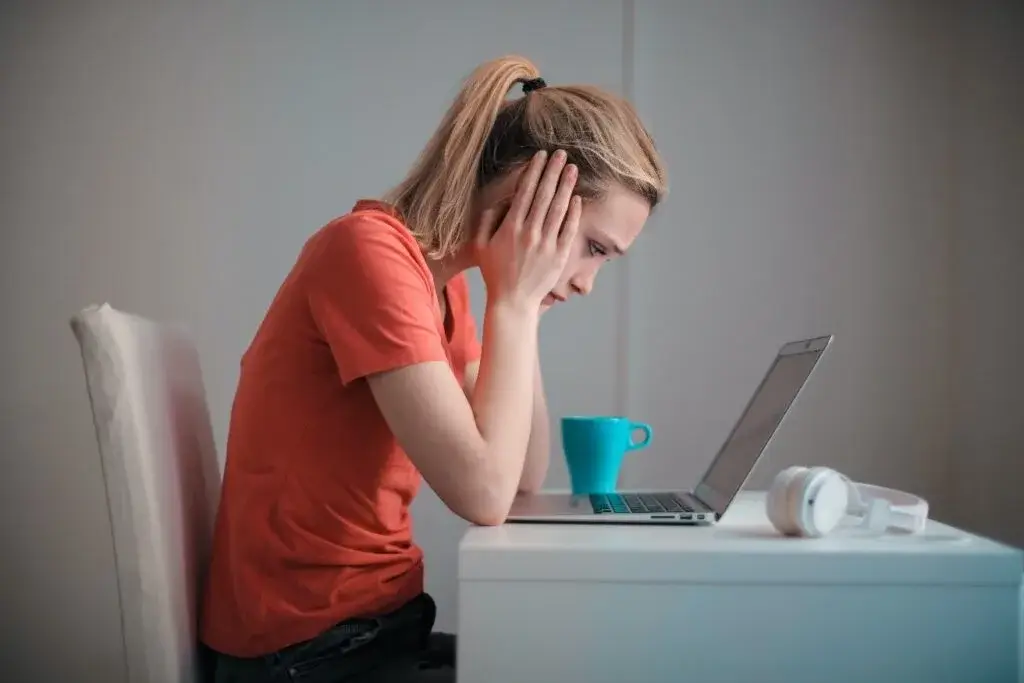 A worried woman sits at a desk looking at her laptop, concerned about obtaining SR-22 insurance after a license suspension.