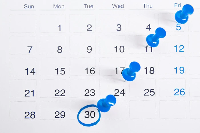 Calendar with blue pushpins marking specific dates, emphasizing an auto policy payment due date circled on the 30th