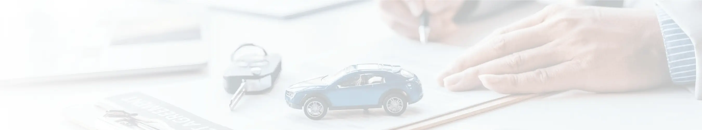 Close-up of a person’s hand writing on paper with a small blue toy car and car keys on the desk