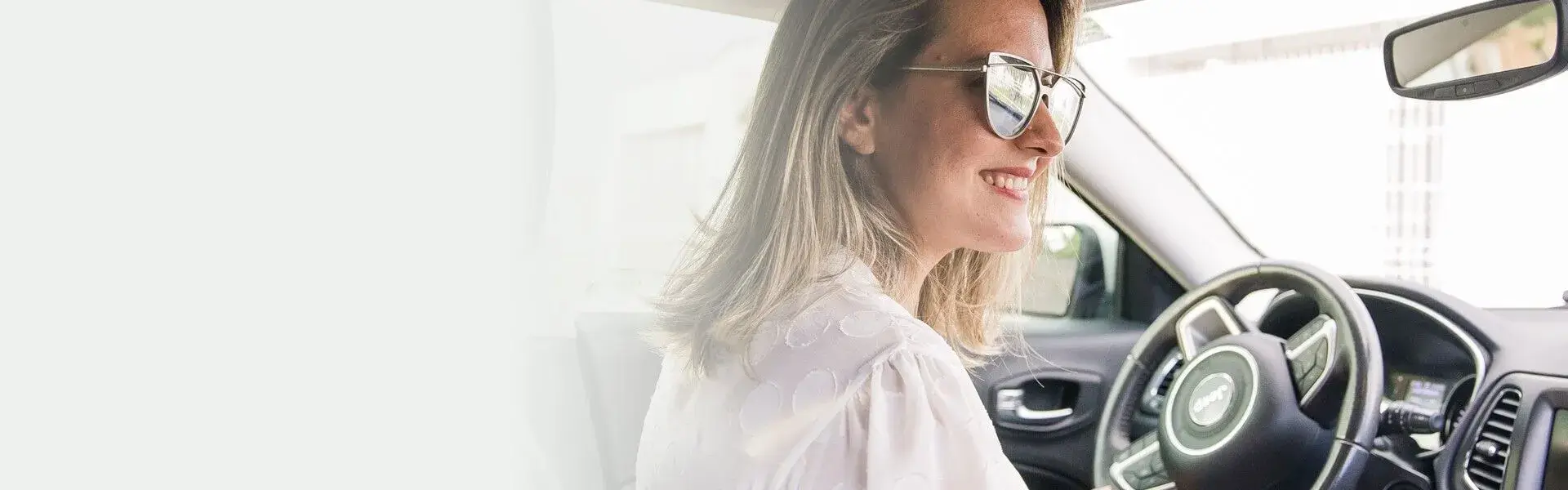 Smiling woman wearing sunglasses seated in the driver’s seat of a car