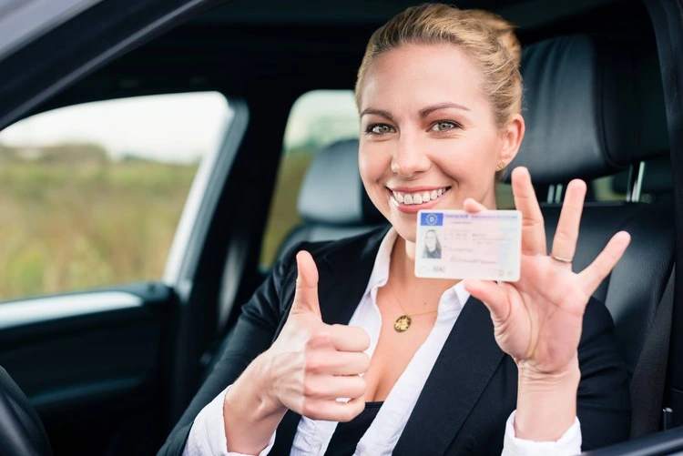 A smiling woman gives a thumbs up while proudly holding her driver's license after regaining her license after a DUI