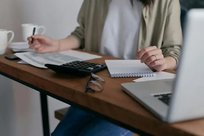 Person sitting at a desk reviewing documents with a calculator, notebook, and laptop