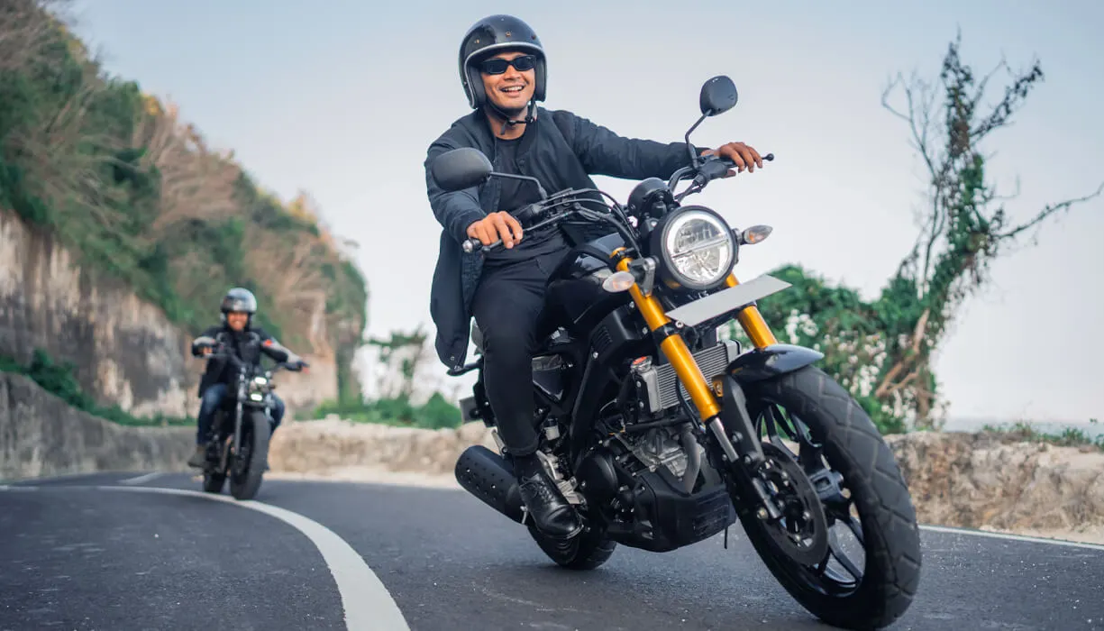 Two motorcyclists driving down a scenic road with rocky cliffs in the background